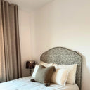 Klassisk sänggavel i tyget Masra framför bäddad säng med beige gardiner och hotellinspirerad styling.