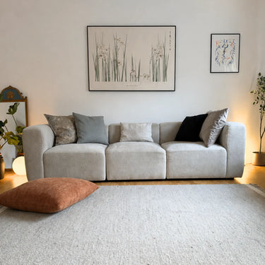 Terrakottafärgad Milena sittkudde i möbeltyg placerad på golvet framför en ljus soffa.