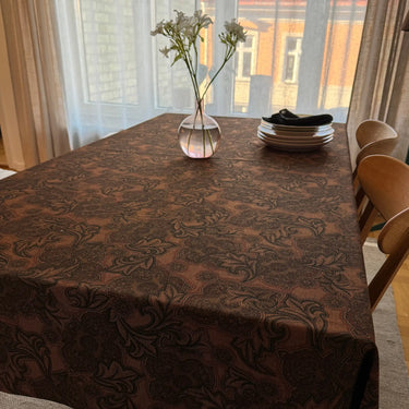 Matbord klätt i tyget Astrid, ett vävt tyg i 50 % viskos och 50 % polyester med klassiskt bladmönster i mustiga jordtoner, stylat som duk i en varm och ombonad miljö.