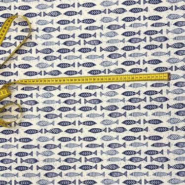 Närbild på bomullstyg med blå fiskar och måttband ovanpå tyget – passar till DIY-projekt, kuddfodral och barnrum.