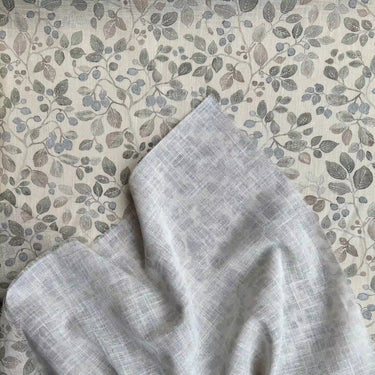Närbild på gardintyg med små blå bär och blad i blå, grå och beige nyanser