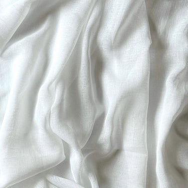 Närbild på gardintyget Emma i vitt, skir polyester med synlig linneliknande struktur och mjuka naturliga veck som visar tygets fall och lätta transparens.