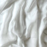 Närbild på gardintyget Emma i vitt, skir polyester med synlig linneliknande struktur och mjuka naturliga veck som visar tygets fall och lätta transparens.