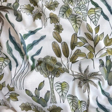 Halvtransparent gardintyg Fiona med stort botaniskt mönster på vit botten i gröna och blågröna nyanser. Tyget visas veckat för att framhäva struktur, fall och färger.