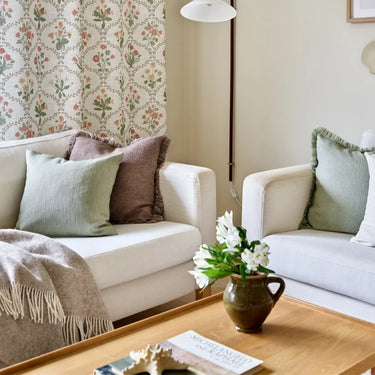 Glasgow ullpläd med fransar draperad över en ljus soffa i ett ombonat vardagsrum
