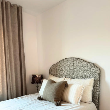 Klassisk sänggavel i tyget Masra framför bäddad säng med beige gardiner och hotellinspirerad styling.