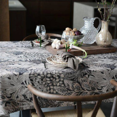 Mönstrad bordsduk med stora blad på ett elegant dukat matbord med porslin, glas och vaser