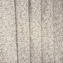 Masra möbeltyg i beige nyans med dekorativt bladmönster, fotograferat i mjuka veck som visar tygets fall och struktur. Slitstarkt tyg för möbler.