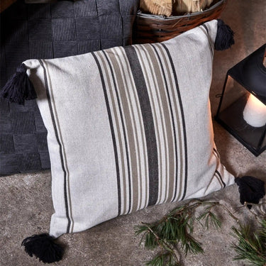 Sunne kuddfodral i svart och beige placerat i en soffa tillsammans med mörka och naturfärgade textilier
