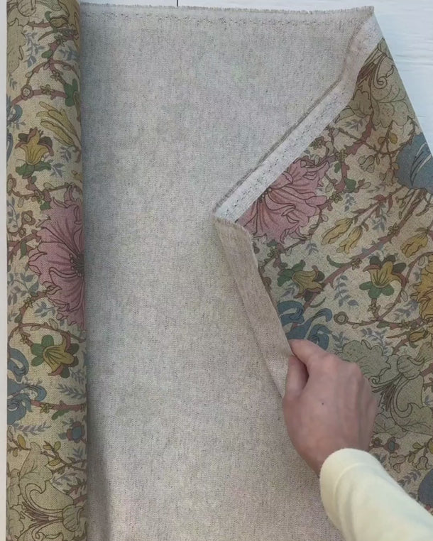 Hand som visar strukturen och baksidan på det mönstrade möbeltyget Anastasia med blommotiv.