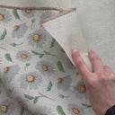 En hand visar och känner på tyget Daisy med prästkragemönster och linnelook för att demonstrera struktur, fall och materialkänsla.