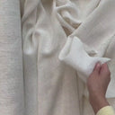 Hand som visar fallet i gardintyget Lova i linnelook och hur det luftiga tyget draperas.