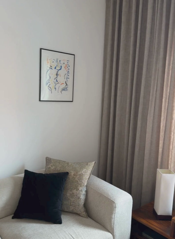 Video som visar den måttsydda beige Nova gardinen från tak till golv i ett vardagsrum, med tygets struktur och mjuka fall.
