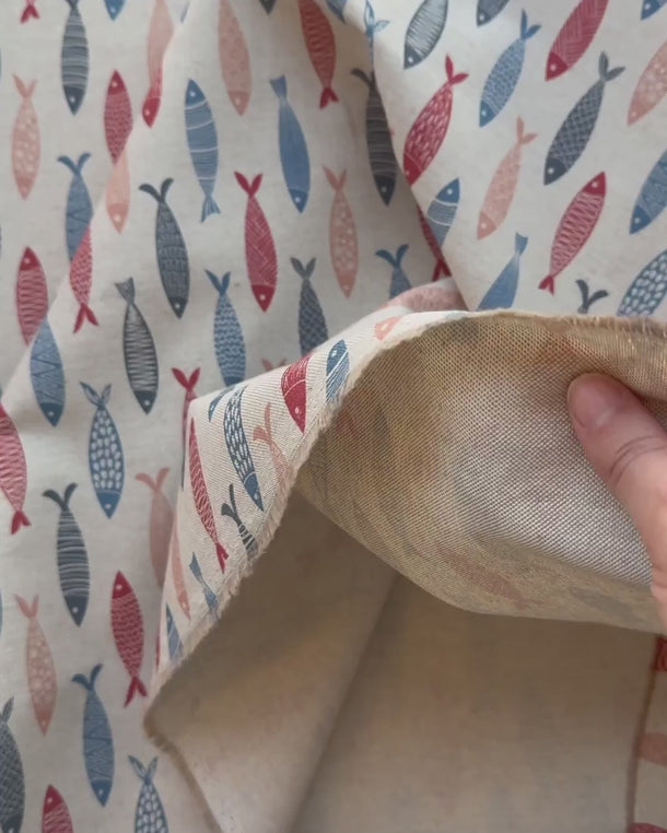 Video som visar Adrian – ett marint tyg med fiskmönster i blå, röda och beige toner. Tygets struktur, färger och mönster visas i rörelse och närbild.